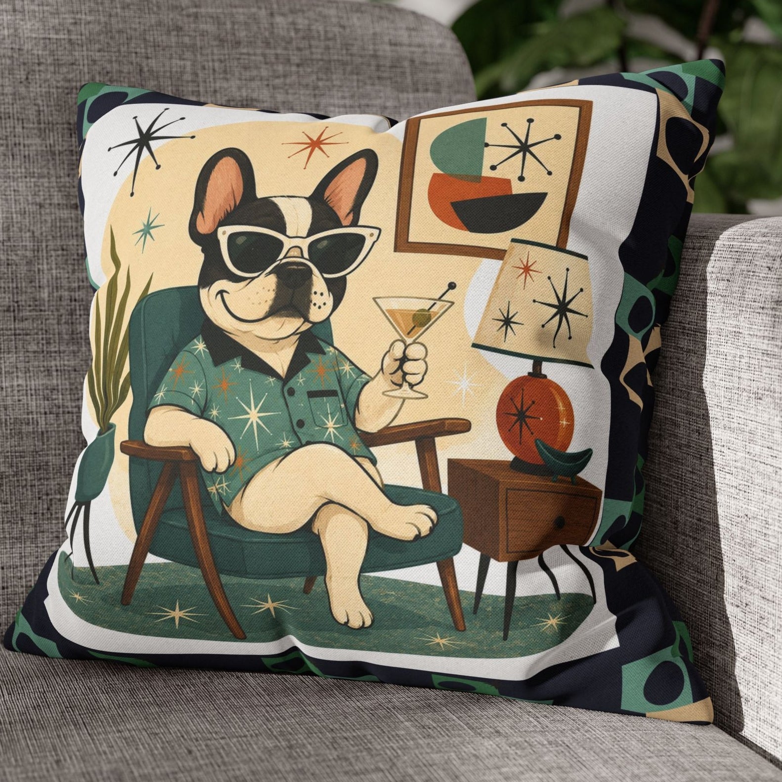 A square decorative throw pillow with a retro 1960s-style illustration of a French bulldog wearing sunglasses and a patterned shirt, sitting on a gray fabric sofa with a blurred houseplant in the background.